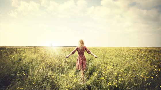 Eine Frau geht durch ein Feld in Richtung Sonne