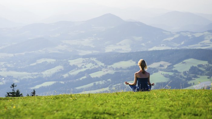 Eine junge Frau meditiert auf einer Weide in den Bergen