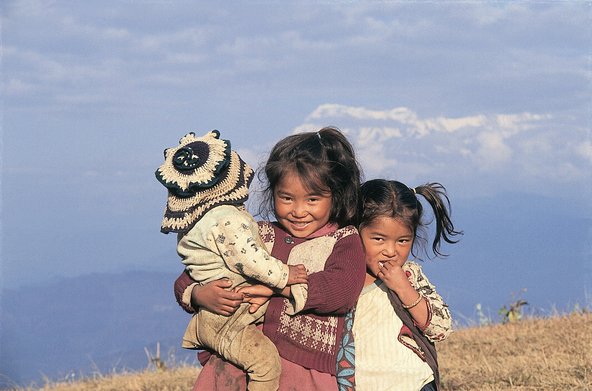 Zwei kleine Mädchen mit Zöpfen und einem Baby im Arm