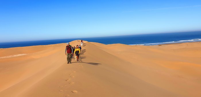 Menschen spazieren auf Sanddünen am Meer