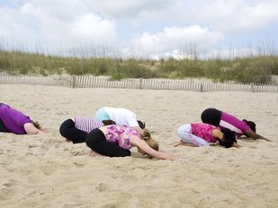 Eine Gruppe an Frauen befindet sind in der Haltung des Kindes am Strand