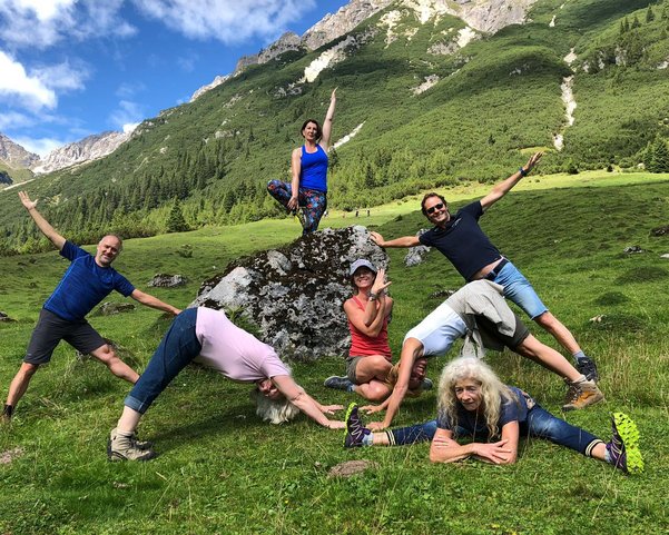 Mehrere Menschen üben Yoga in den Bergen