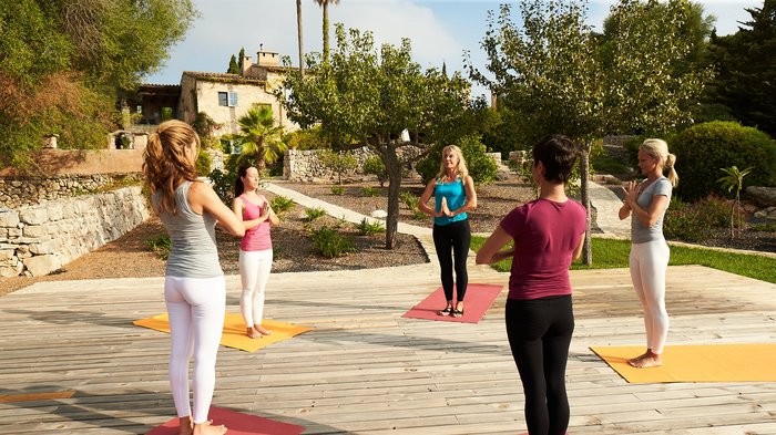 Eine Gruppe an Frauen übt Yoga auf einer Terasse im Garten