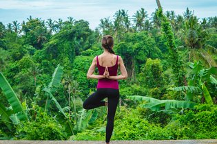 Sportlich gekleidete Frau in Yogapositon vor einem Dschungel