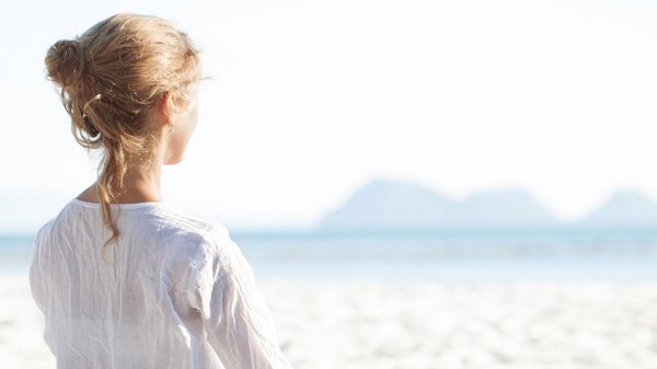 Eine junge Frau sitzt meditierend an einem weißen Strand