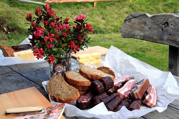 Ein Tisch gedeckt mit Käse, Wurst, Brot und Blumen