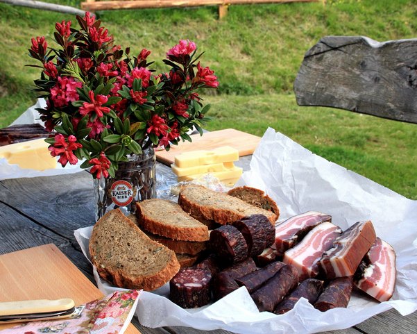 Ein Tisch gedeckt mit Käse, Wurst, Brot und Blumen