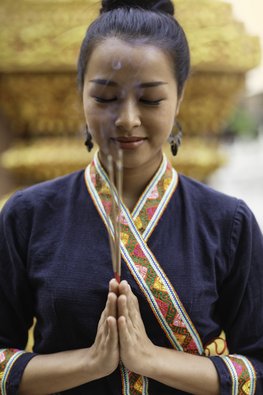 Eine Frau in traditionellen Kleidern befindet sich in einer Position zum beten mit Räucherstäbchen