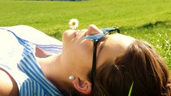 Eine junge Frau entspannt sich auf einer Wiese mit einer Gänseblume im Mund