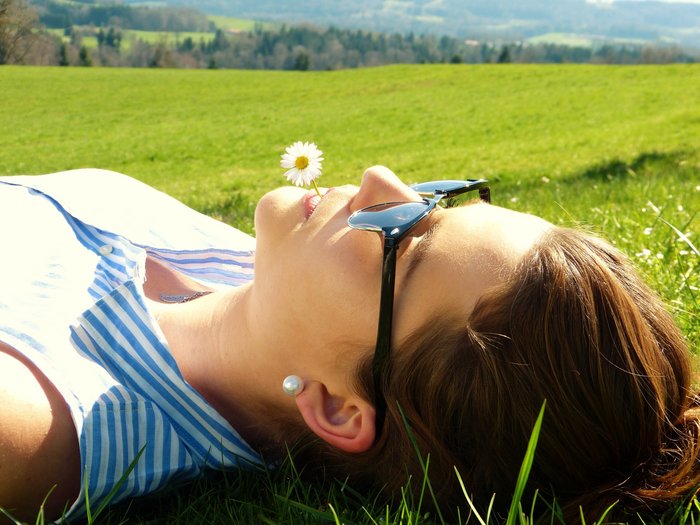 Eine junge Frau entspannt sich auf einer Wiese mit einer Gänseblume im Mund 