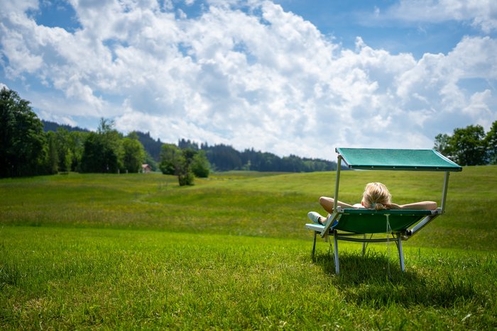 Eine Frau liegt auf einer grünen Weide und sonnt sich auf einer Sonnenliege
