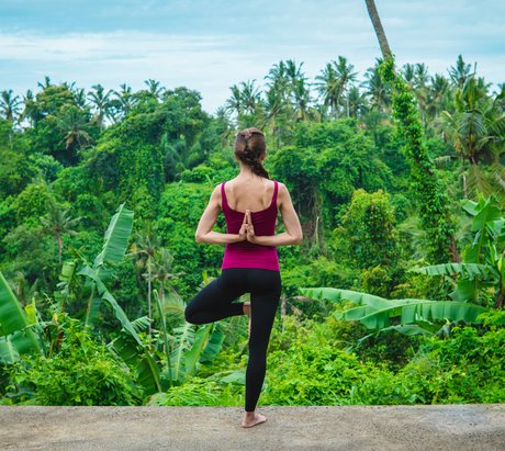 Sportlich gekleidete Frau in Yogapositon vor einem Dschungel