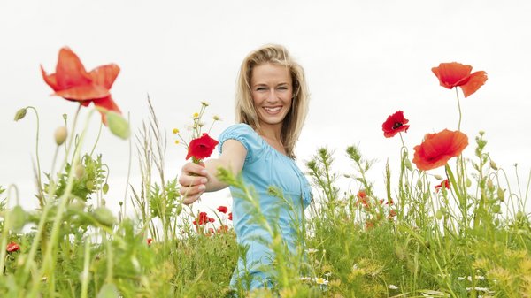 Eine Frau steht in einem Blumenfeld mit einer Blume in der Hand