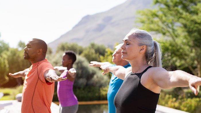Eine Gruppe an älteren Menschen übt Yoga mit ausgestreckten Armen
