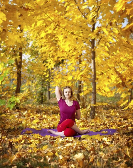 Frau sitzt in Yoga-Pose in einem herbstlichen Wald