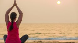 Eine Frau übt Yoga bei Sonnenuntergang am Meer