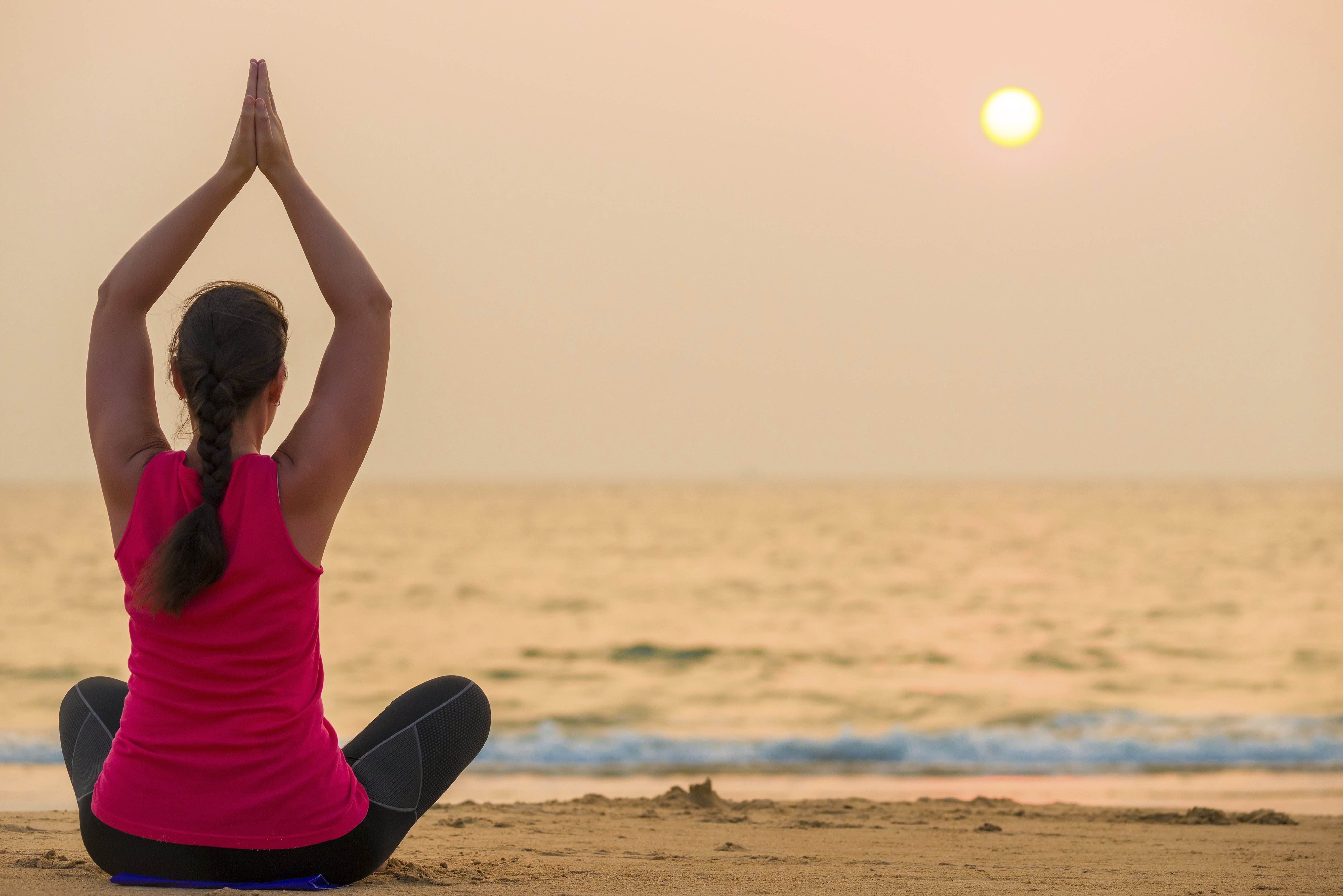 Eine Frau übt Yoga bei Sonnenuntergang am Meer