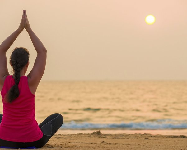 Eine Frau übt Yoga bei Sonnenuntergang am Meer