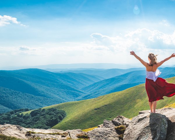 Eine Frau steht auf einem Felsen mit Blick auf eine bergige Landschaft