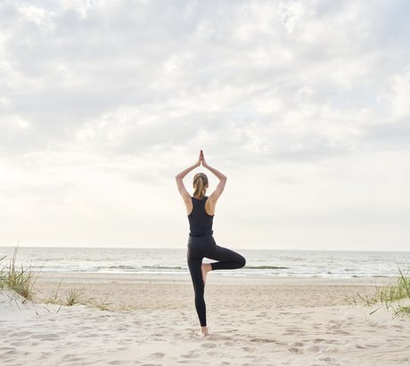 Eine Frau in der Baum Pose am Strand