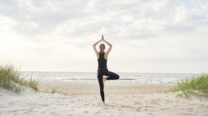 Eine Frau in der Baum Pose am Strand