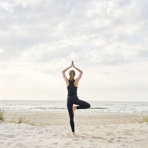 Eine Frau in der Baum Pose am Strand