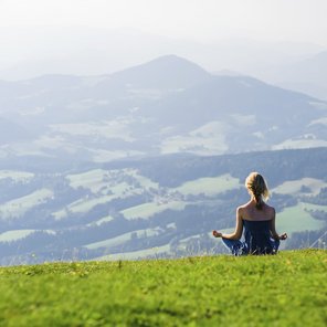 Eine junge Frau meditiert auf einer Weide in den Bergen