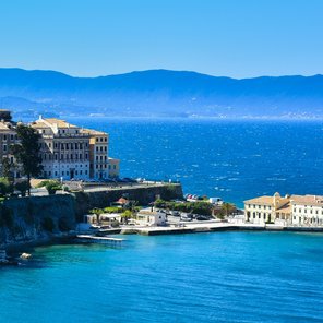 Eine Stadt mit weißen Gebäuden vor Bergen und blauem Meer auf den Überbleibseln einer alten Festung