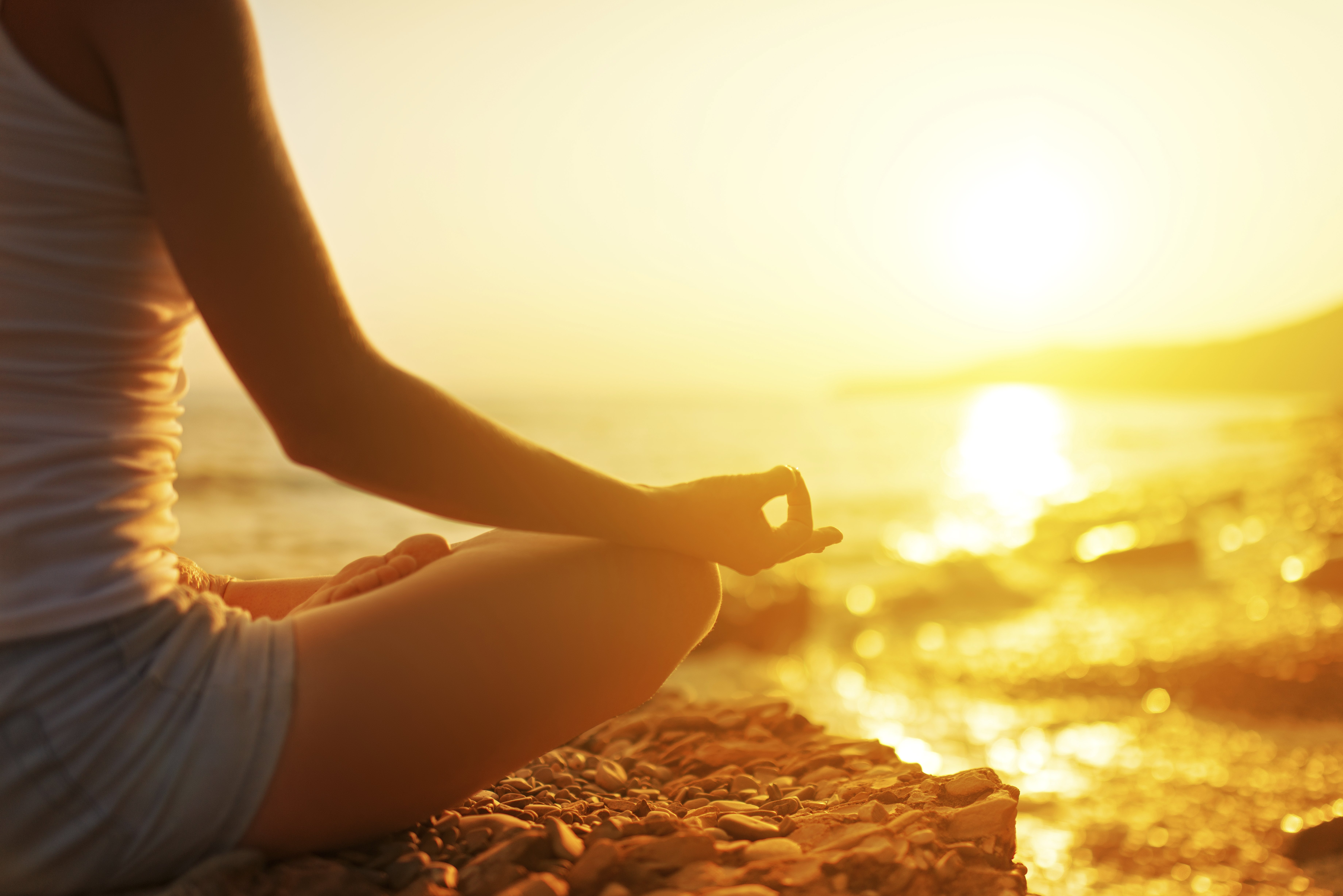 Eine Frau meditiert bei Sonnenuntergang auf einem Felsen am Meer