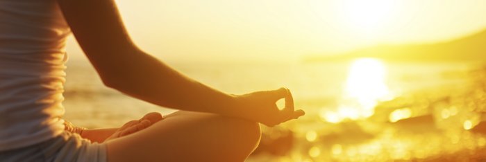 Eine Frau meditiert bei Sonnenuntergang auf einem Felsen am Meer