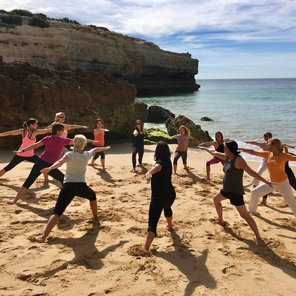 Frauen in einem Kreis am Strand in der Pose Krieger 2