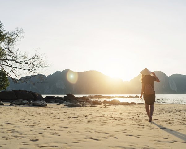 Eine Frau mit einem asiatischen Kegelhut spaziert am Strand