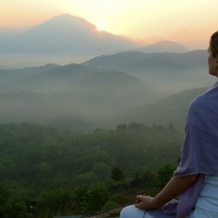 Eine Frau übt Meditation mit Aussicht auf die Berge bei Sonnenaufgang