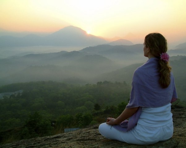 Eine Frau übt Meditation mit Aussicht auf die Berge bei Sonnenaufgang