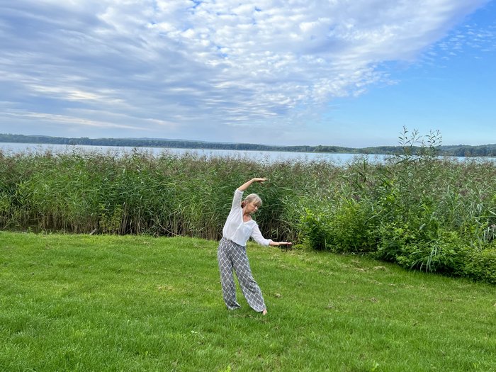 Frau übt Qi Gong auf einer Wiese am See