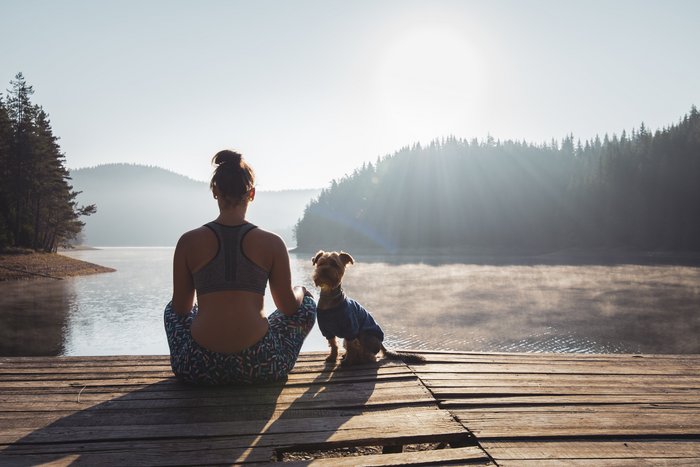 Frau meditiert mit Hund an einem See