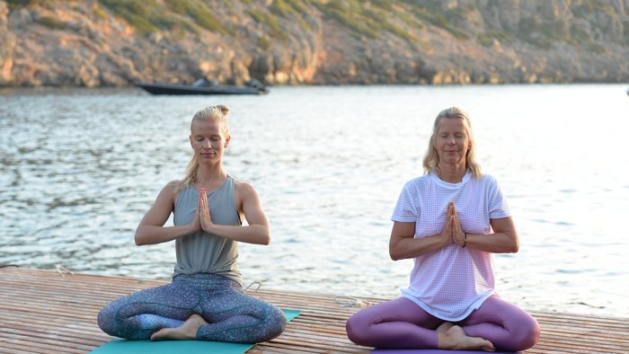 Zwei blonde Frauen sitzen in Meditationshaltung auf einem Steg am Meer