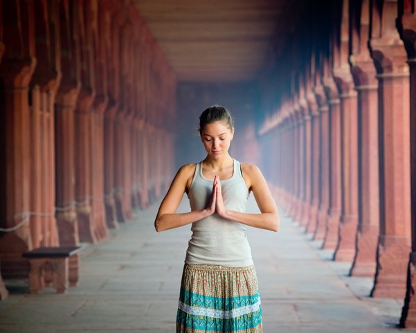 Eine junge Frau steht in einem Tempel die Hände im anjali mudra