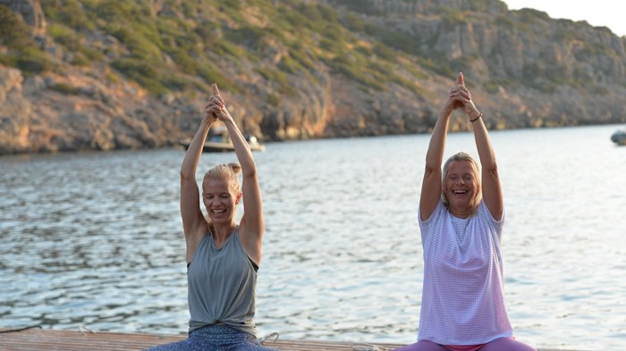 Zwei Frauen üben Yoga auf einem Steg am Meer