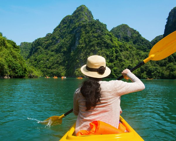 Eine Frau mit Hut und rosa Pullover sitzt in einem gelben Kayak und paddelt