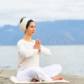 Eine Frau übt Meditation an einem See in weißer Bekleidung