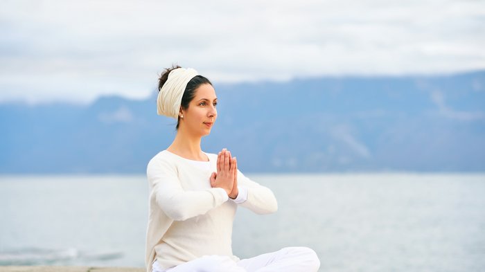 Eine Frau übt Meditation an einem See in weißer Bekleidung