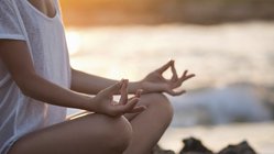 Ein junges Mädchen meditiert auf einem Felsen am Meer