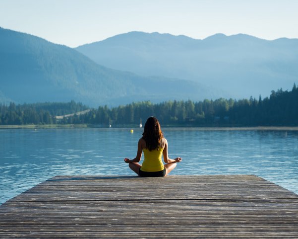 Frau meditiert in den Bergen auf einem Steg zum See