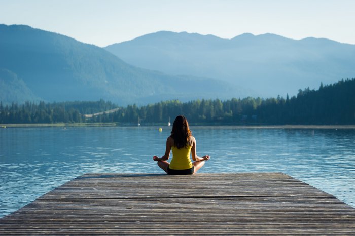 Frau meditiert in den Bergen auf einem Steg zum See