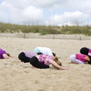 Eine Gruppe an Frauen befindet sind in der Haltung des Kindes am Strand