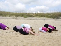 Eine Gruppe an Frauen befindet sind in der Haltung des Kindes am Strand