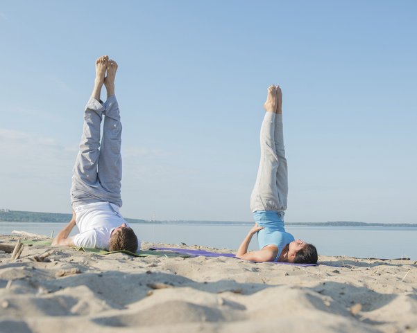 Ein junges Pärchen übt Yoga am Strand