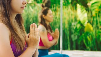 zwei Frauen im Schneidersitz und die Hände im Anjali Mudra