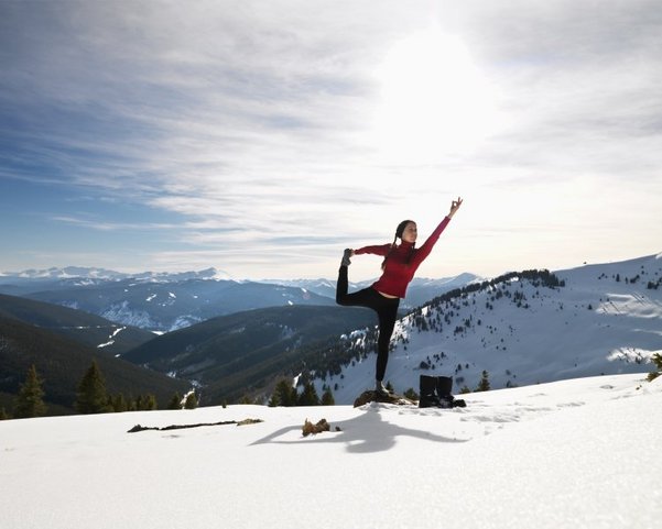 Junge Frau, die Yoga macht, posiert auf Felsen im Schnee in bergigem Gelände